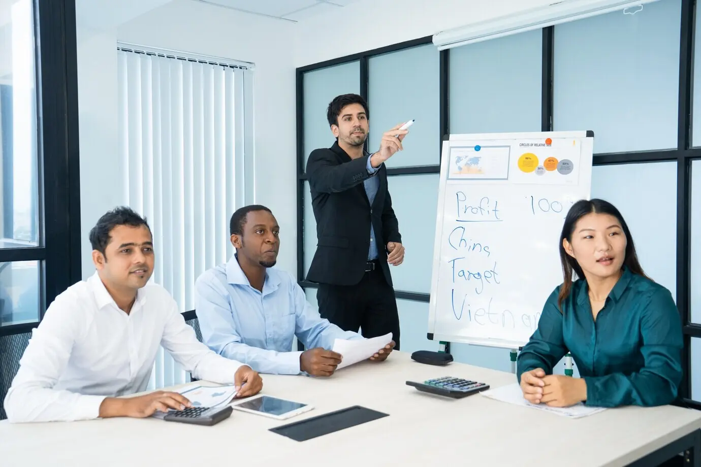 Presentador serio y atractivo señalando hacia un lado mientras explica datos en una reunión.